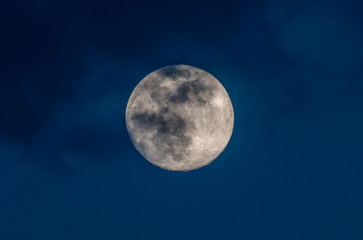 gorgeous full moon in a dark blue night sky gets covered by soft wispy dark clouds