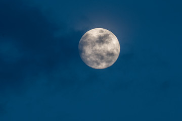 Fototapeta na wymiar gorgeous full moon in a dark blue night sky gets covered by soft wispy dark clouds