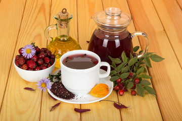 Pitcher of broth hips, dried fruits in bowl, branch with berries and leaves, on wooden table