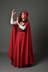 full length portrait of woman wearing red fantasy costume with cloak, standing pose on grey studio background.
