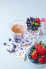 A glass of coffee and pudding chia with blueberries and strawberries for breakfast. Vegetarian food. A small bouquet of flowers and a blue background. Vertical photo