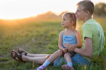 Two children are sitting on the grass in the evening