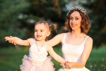 Mom and daughter are two years old sitting on the grass in the park