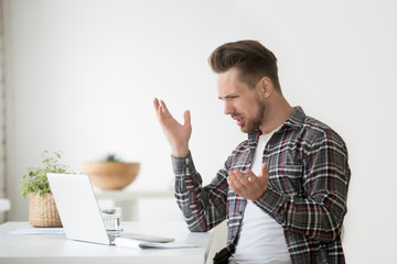Confused angry young man frustrated by online problem, casual businessman looking at stuck laptop...