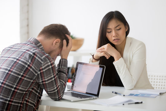 Stressed sad multi-ethnic partners searching problem solution at meeting, asian and caucasian colleagues depressed by business failure or bad news, feeling shocked desperate about company bankruptcy