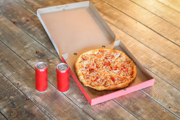 slice pizza in box and can of soda on wood background