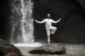 Man standing in meditation yoga on rock at waterfall