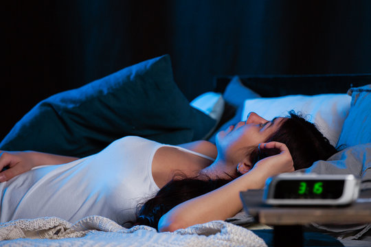 Image of young woman with insomnia lying on bed next to clock