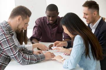 Multiracial millennial team helping in assembling puzzle, creative smiling diverse people group connected in finding best business solution together, good successful teamwork and teambuilding concept