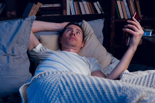 Picture of man with sleeplessness with phone in hands lying in bed