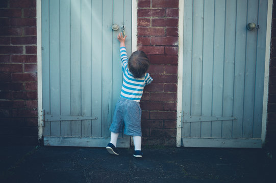 Toddler reaching for door handle in yard