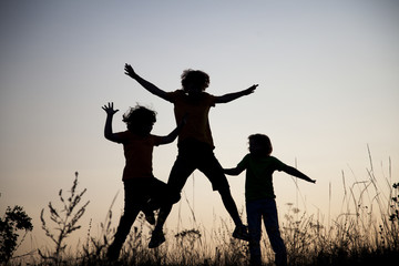 Fototapeta na wymiar Children playing jumping on summer sunset meadow silhouetted