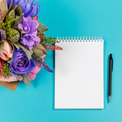 Artificial handmade flowers, a notebook and a black pen on a blue background
