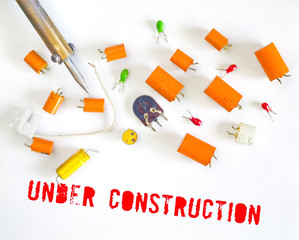 Website under construction message with defective capacitors and soldering iron, symbol