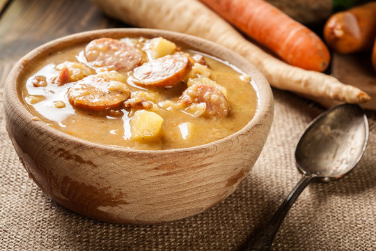 Wooden bowl of split pea soup with sausage and potatoes