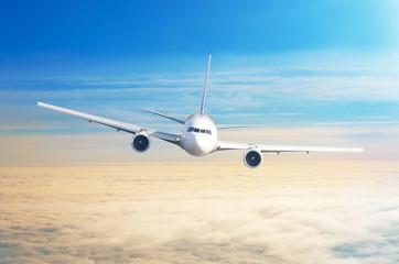 Passenger airplane flying at flight level high in the sky above overcast clouds and blue sky.