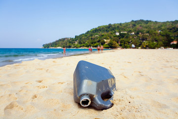An empty plastic canister is lying on the sand of the resort beach.