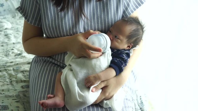 Mother feeding the baby with baby bottle in the living room