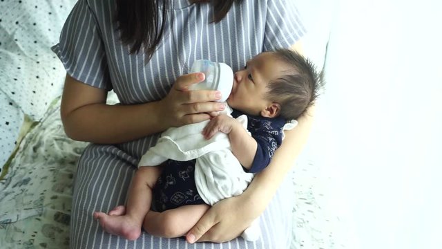 Mother feeding the baby with baby bottle in the living room