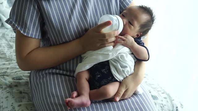 Mother feeding the baby with baby bottle in the living room