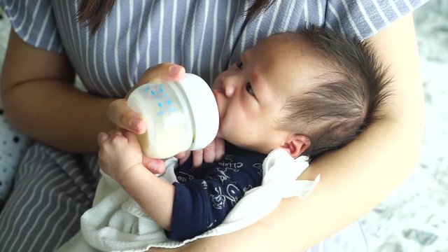 Mother feeding the baby with baby bottle in the living room