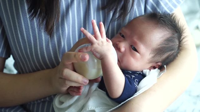 Mother feeding the baby with baby bottle in the living room