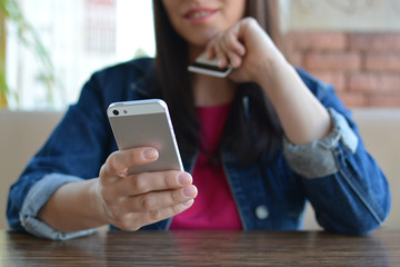 A brunette girl in a denim jacket is eating lunch in a cafe and using her phone. Communication through messenger. Casual loose clothing.