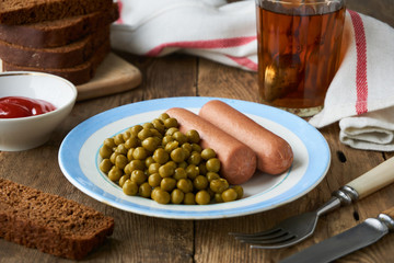 Boiled sausages with canned green peas on a plate
