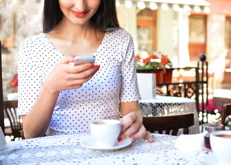 Attractive woman in a street cafe with a phone. A girl at a lunch break drinks coffee and communicates through the messenger with her smartphone. The Internet. Message.