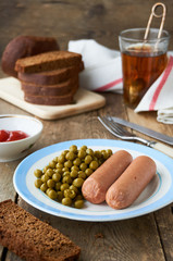 Boiled sausages with canned green peas on a plate
