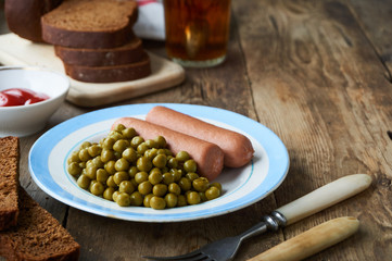 Boiled sausages with canned green peas on a plate