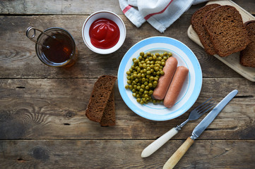Boiled sausages with canned green peas on a plate