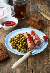 Boiled sausages with canned green peas on a plate
