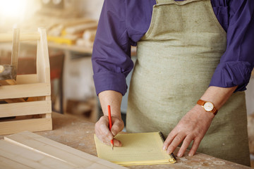 close up cropped photo of old builder with white beard and moustache writing the plan of...