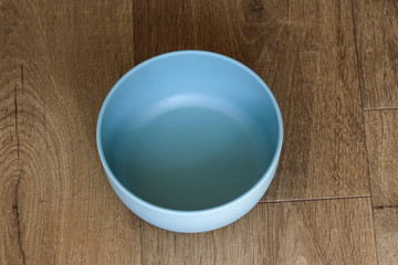 Empty blue plastic bowl on wooden background, above view