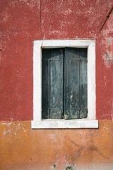 Verfallene Fensterläden vor rot oranger weisser Wand