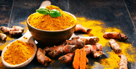 Composition with bowl of turmeric powder on wooden table