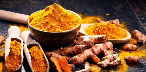Composition with bowl of turmeric powder on wooden table