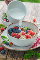 Pouring milk into granola with fresh blueberries and raspberries