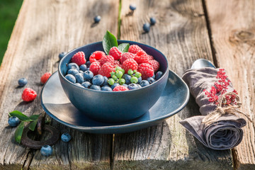 Fresh and tasty berries in blue bowl on rustic table