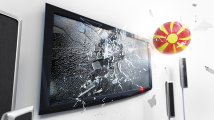 Soccer ball with the flag of Macedonia kicked through a shattering tv screen.(3D rendering series)