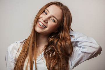 Happy young red-haired woman in braces smiling on white background looking at camera - obrazy, fototapety, plakaty