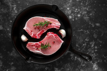 Raw Pork Loin chops in rustic skillet, pan with rosemary, garlic, pepper. top view. background