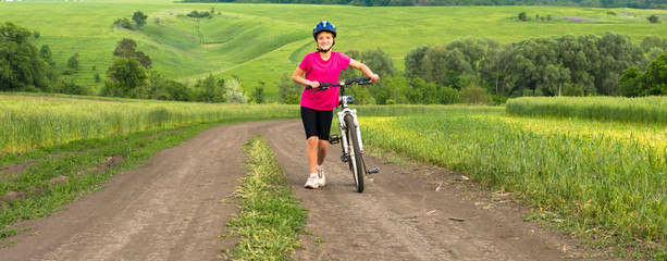 Sporty girl with bicycle in green field.