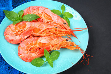 Large royal raw frozen prawns on a blue plate with thyme and basil on a concrete table. Red shrimps. Top view.