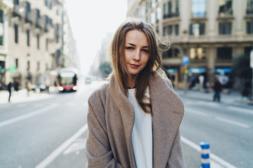 Half length portrait of a beautiful caucasian female with long blonde hair wearing trandy outfit smiling at the camera while standing on a blurred city street background on a warm spring day.