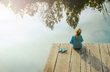 Lonely small girl sitting near river. Riskily situation