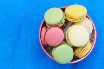 Colorful macaroons in bowl on vivid blue surface with copy space
