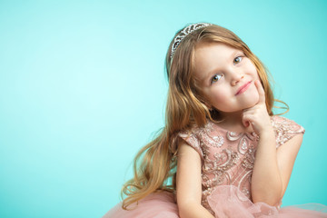 Adorable little child girl face closeup portrait in princess dress looking at camera isolated on blue background © alfa27