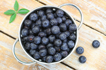 Fresh blueberries in aluminum colander on rustic wooden surface
